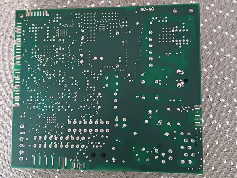 Cara de soldaduras de una placa electrónica verde, con puntos de soldadura y pistas, sobre un salvamanteles plateado